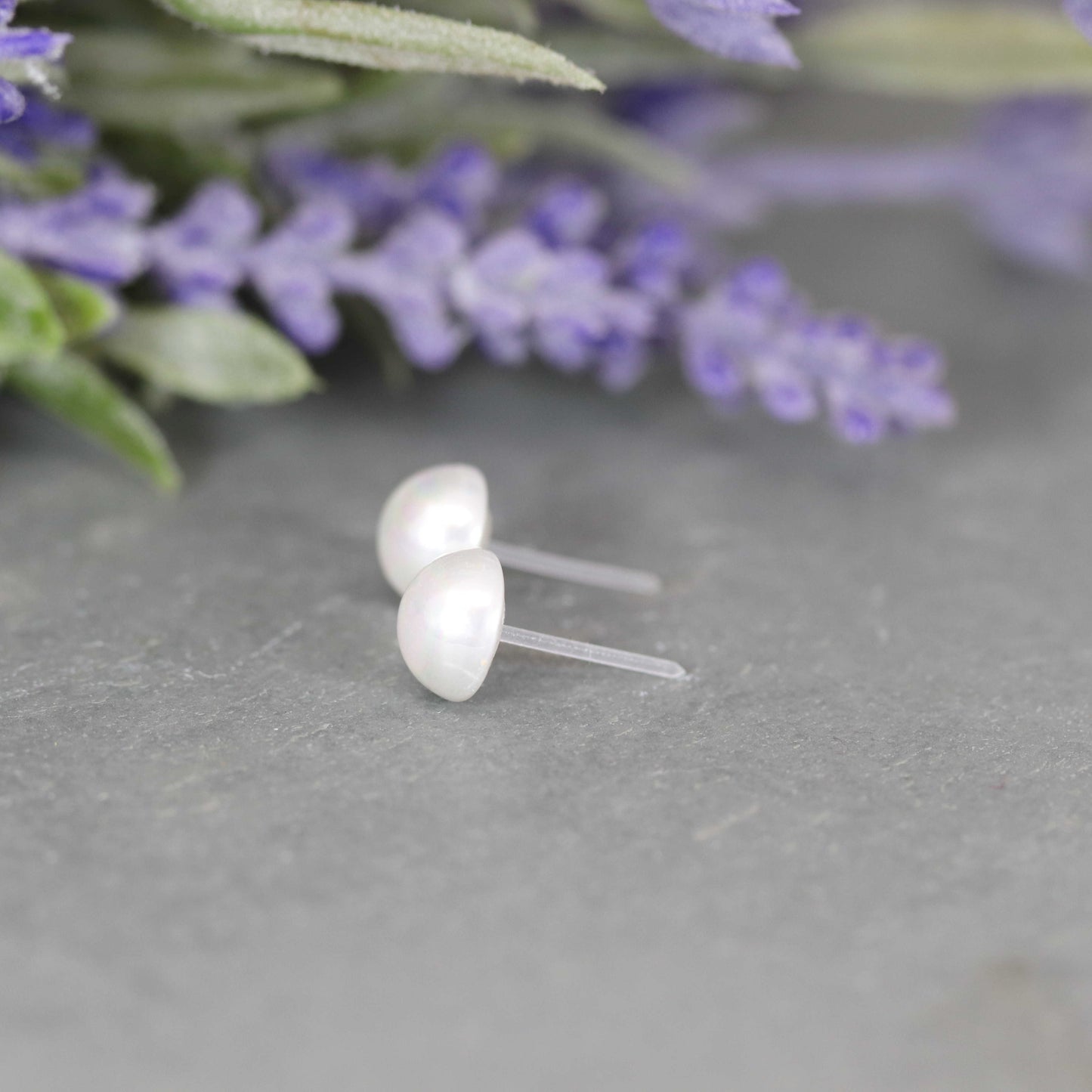 A pair of white-colored cabochon shell stud pearl earrings displayed on a gray surface, with the earrings appearing with a white pearl-like finish.