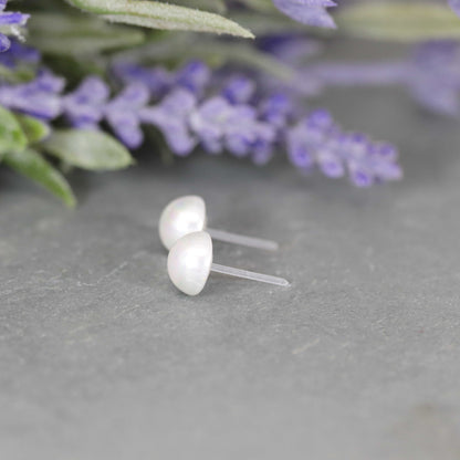 A pair of white-colored cabochon shell stud pearl earrings displayed on a gray surface, with the earrings appearing with a white pearl-like finish.