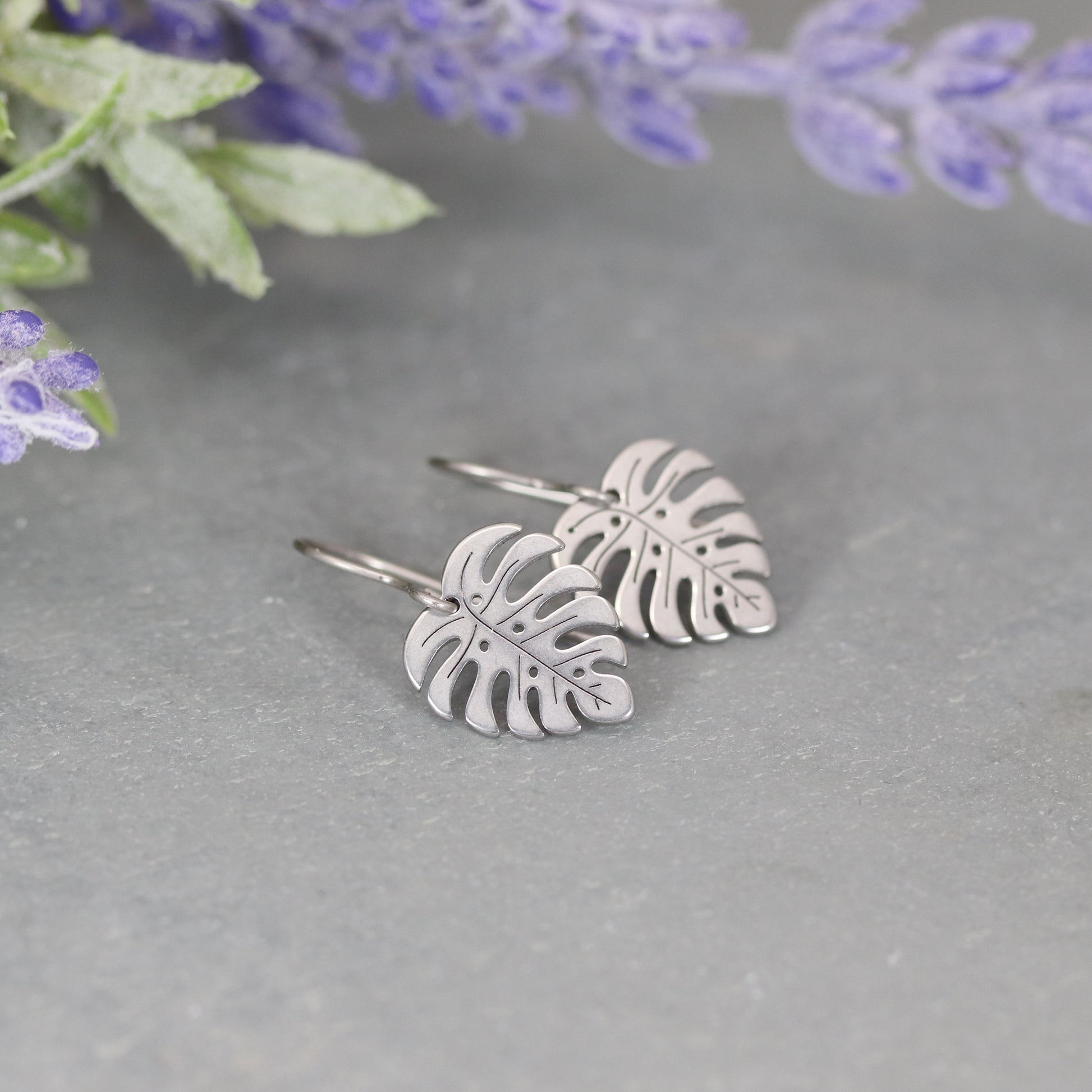 A pair of gold-colored dangle earrings designed to resemble Monstera leaves.