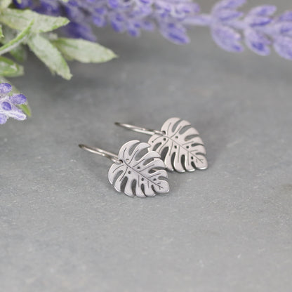 A pair of gold-colored dangle earrings designed to resemble Monstera leaves.