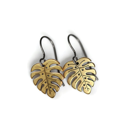 A pair of gold-colored dangle earrings designed to resemble Monstera leaves.