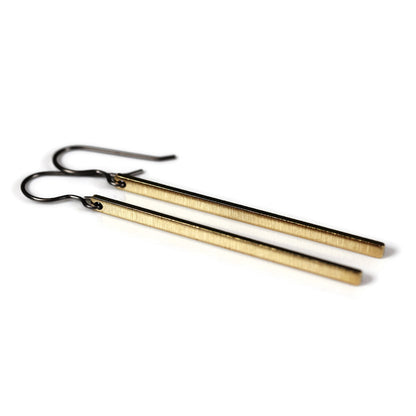 A pair of long brushed minimalist bar dangle earrings in gold color with black plastic hooks.
