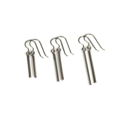 A set of three dangle earrings with bar hooks, made of brushed raw brass, displayed against a white background.