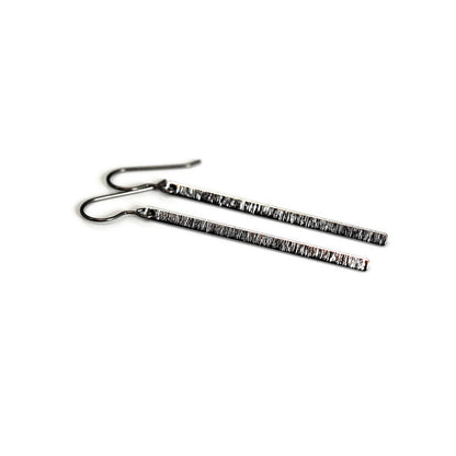 A pair of long brushed minimalist bar dangle earrings in gold color with black plastic hooks.