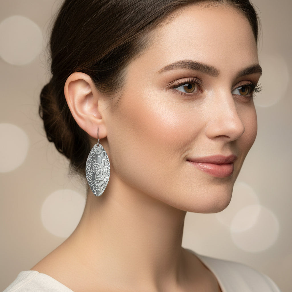 A pair of silver floral embossed twisted oval dangle earrings placed on a white surface.