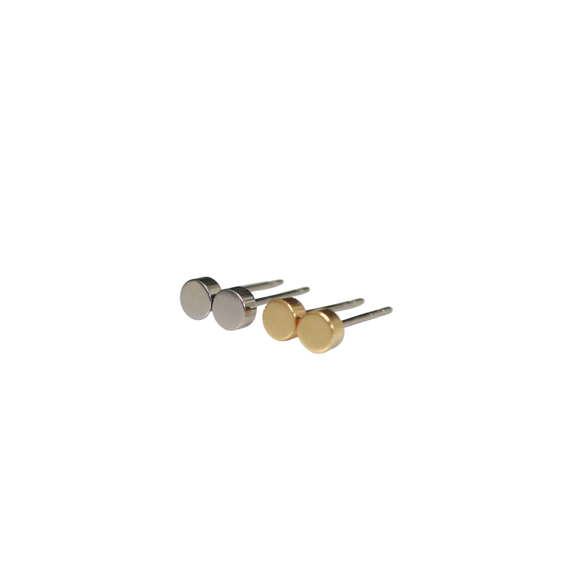 A pair of round dot stud earrings in silver and gold colors, placed on a white surface with foliage in the background.