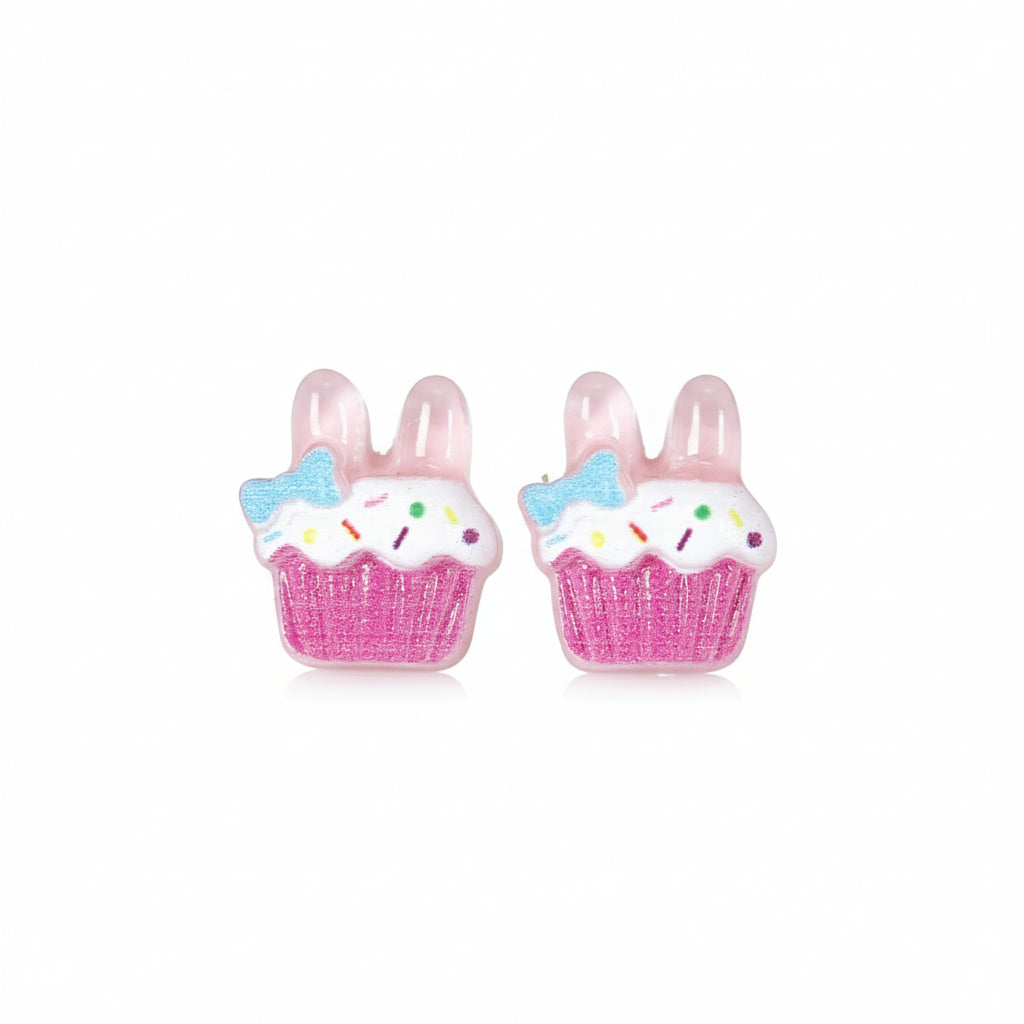 A pair of pink cupcake-shaped stud earrings with bunny ear designs, adorned with white and blue accents, displayed on a reflective surface.