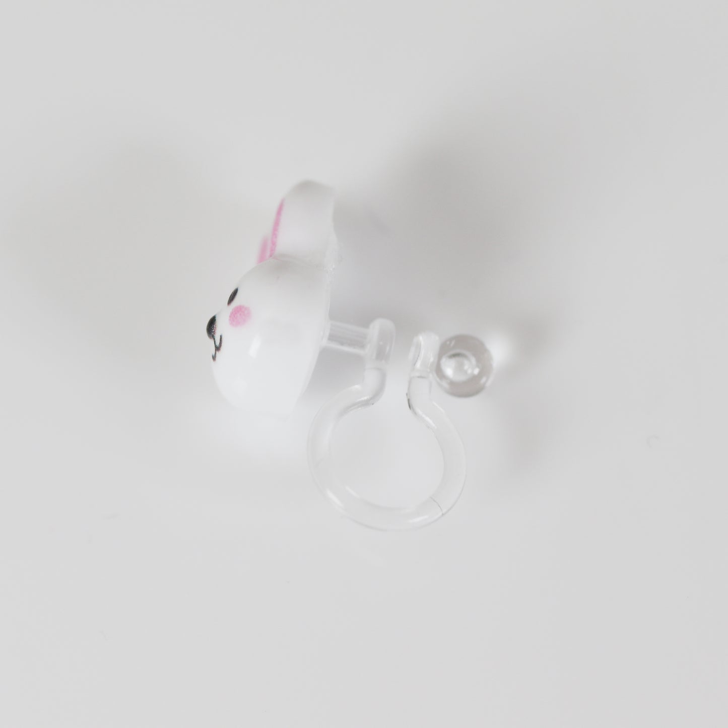 A pair of white bunny face stud earrings with pink inner ears and black eyes, attached to clear posts.