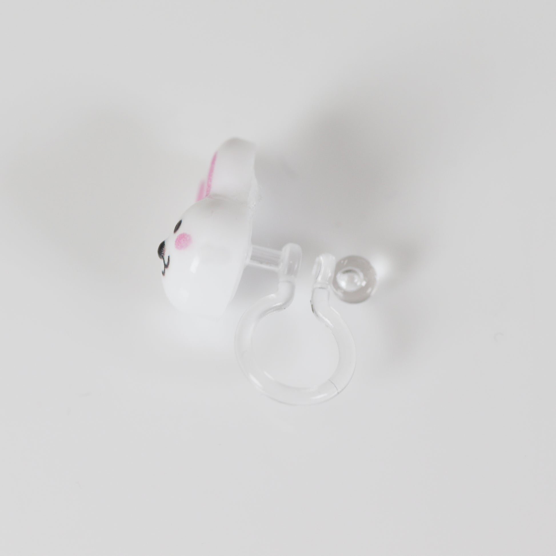A pair of white bunny face stud earrings with pink inner ears and black eyes, attached to clear posts.