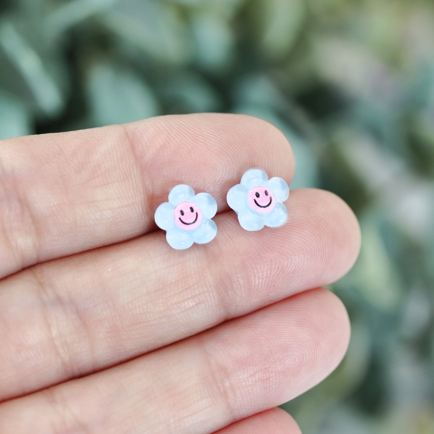 A pair of blue smiley face flower stud earrings displayed with a "More Colors" text overlay.