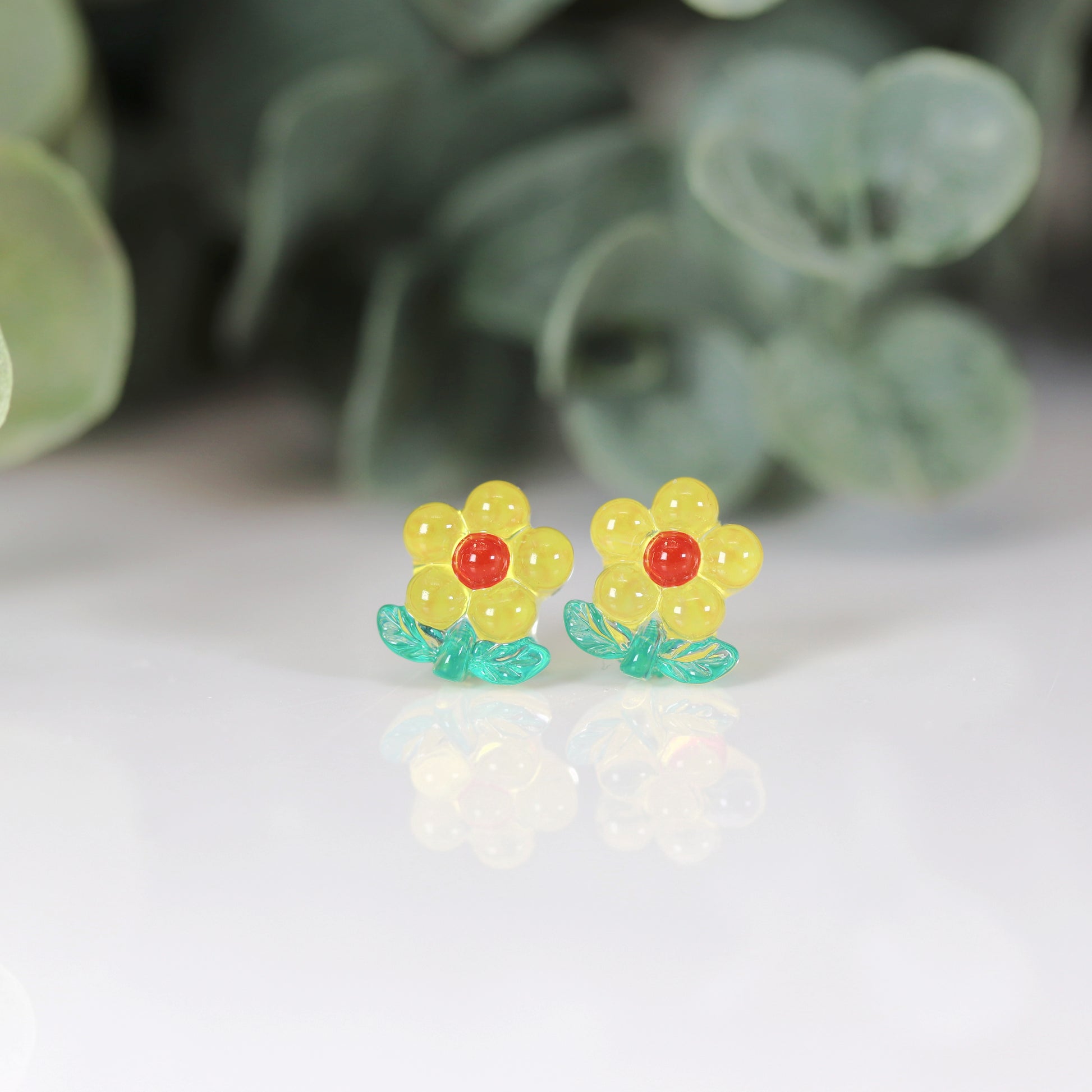 A set of colorful flower stem stud earrings displayed in a row, with colors including pink, blue, green, and yellow.
