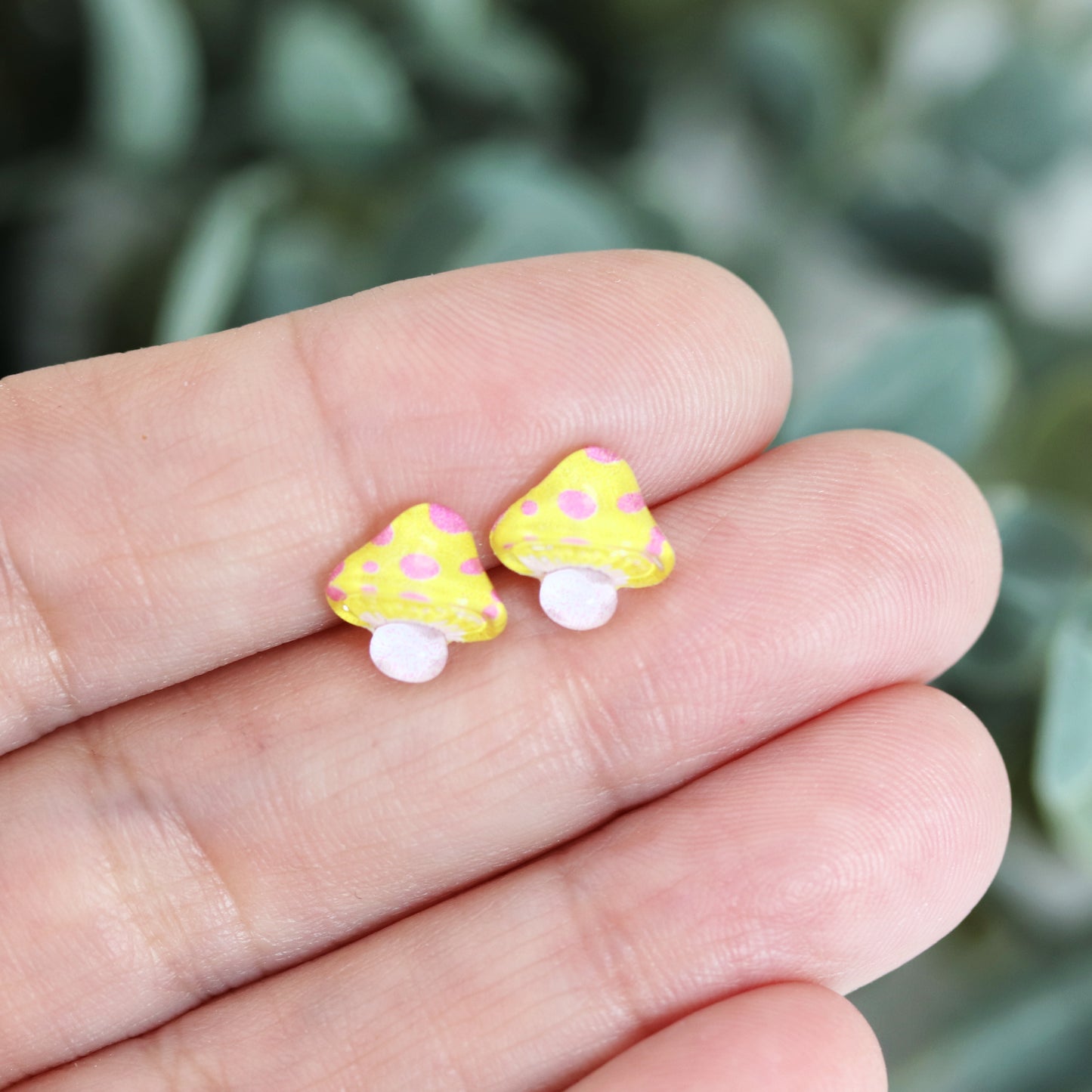 A set of colorful mushroom stud earrings in various colors displayed in a hand