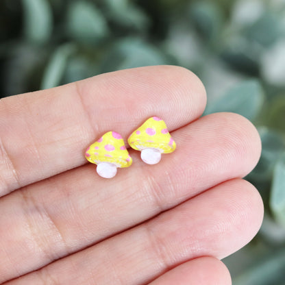 A set of colorful mushroom stud earrings in various colors displayed in a hand